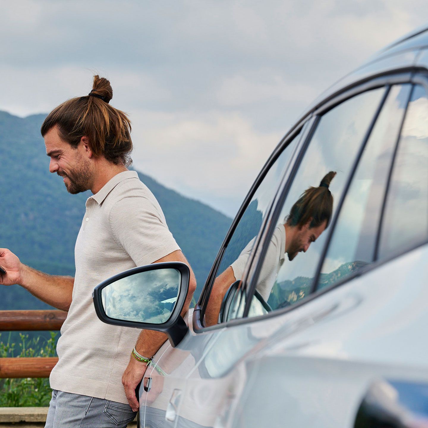 Ein Mann lehnt an einem Volkswagen ID. und blickt auf sein Smartphone.