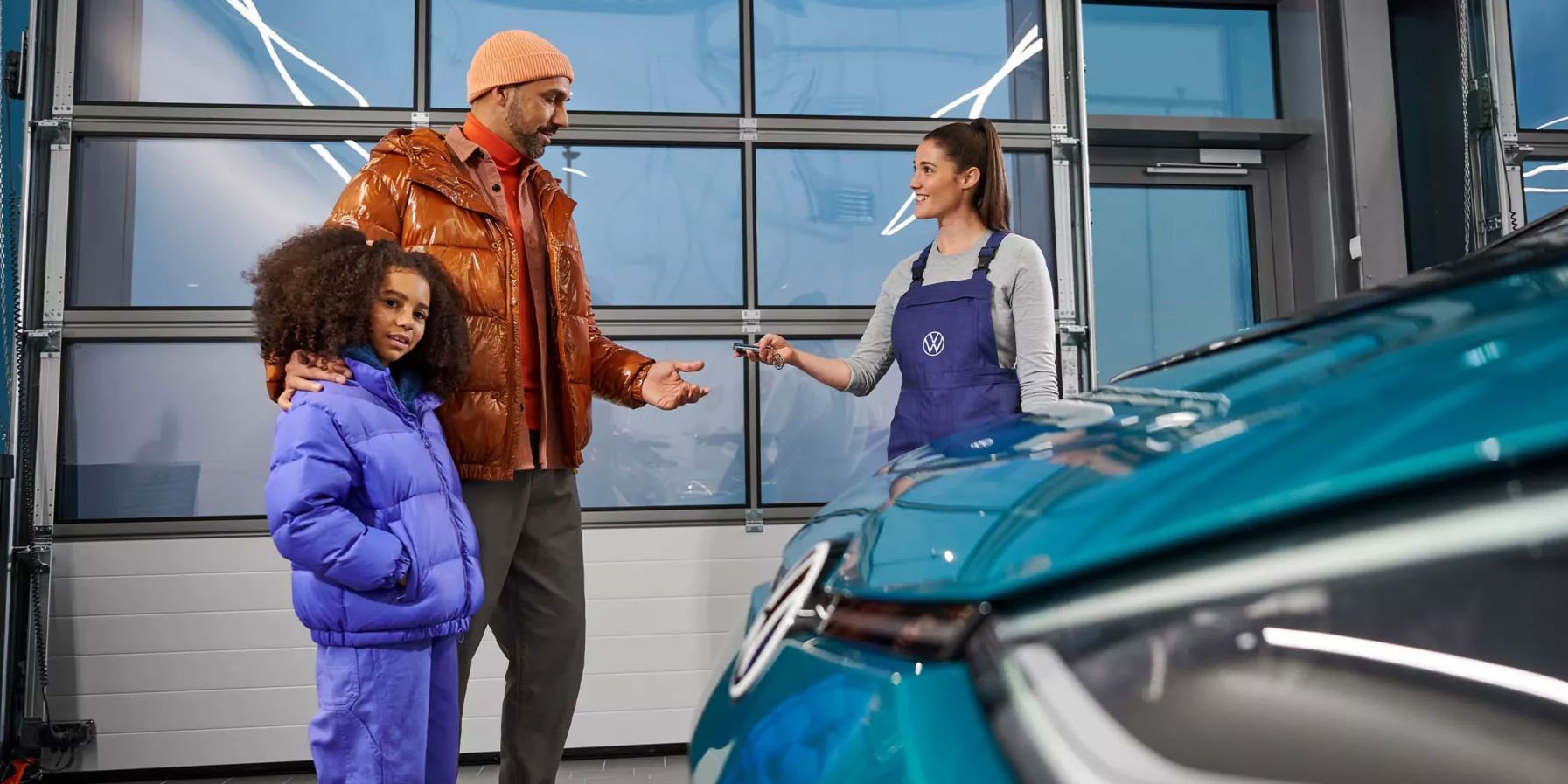 Eine VW Service Technikerin übergibt die Fahrzeugschlüssel an einen Mann mit Kind