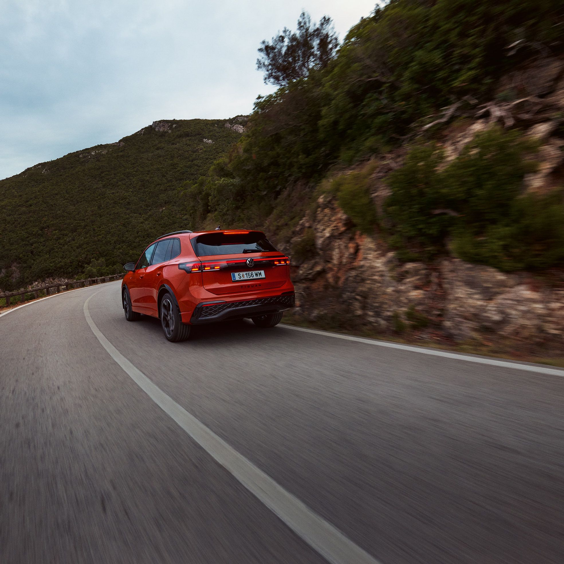 Roter VW Tiguan in Heckansicht fährt durch eine bergige Landschaft.