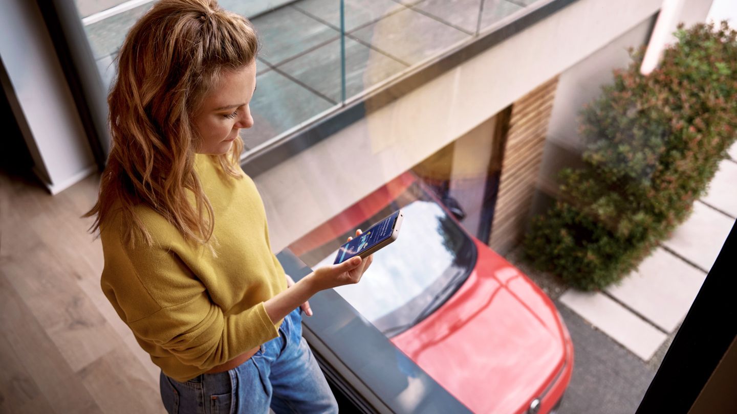 Frau schaut zu Hause auf ihr Smartphone, während ihr Tiguan in der Einfahrt geparkt ist