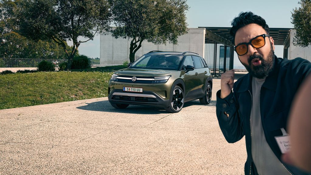 Ein Mann macht ein Selfie mit einem grünen VW ID. Cross, der auf der Auffahrt eines Gebäudes parkt.