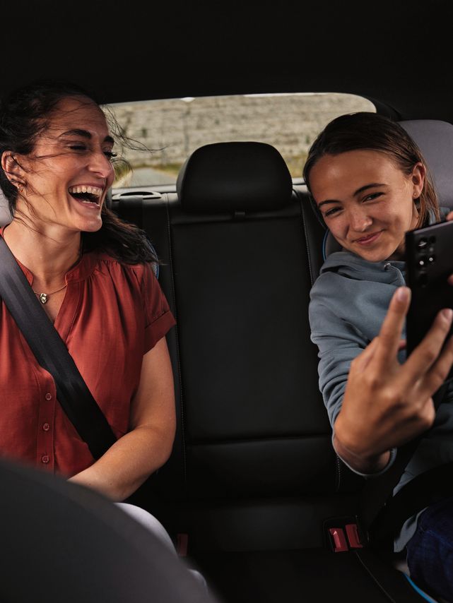 2 Peronen sitzen auf der Rückbank eines Volkswagen und schauen lächelnd auf ein Mobiltelefon