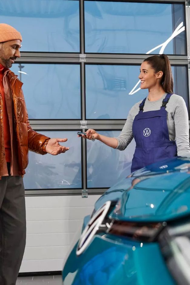 Eine VW Service Technikerin übergibt die Fahrzeugschlüssel an einen Mann mit Kind