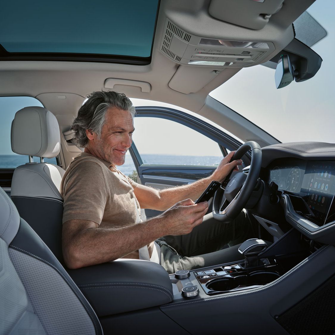 Ein Mann in einem parkenden VW Touareg Elegance verbindet sein Smartphone per Wireless App Connect mit dem VW Touareg Elegance.