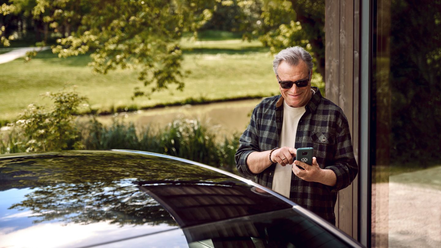 Ein Mann steht hinter einem VW und hält ein Handy in der Hand.  