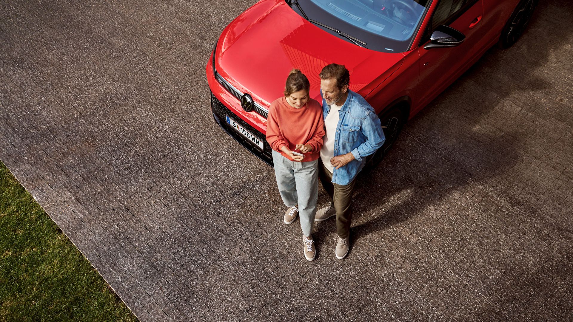 Eine Frau und ein Mann stehen vor einem Tiguan und schauen gemeinsam auf ein Handy.