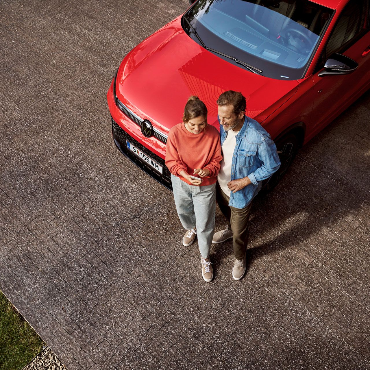Eine Frau und ein Mann stehen vor einem Tiguan und schauen gemeinsam auf ein Handy.