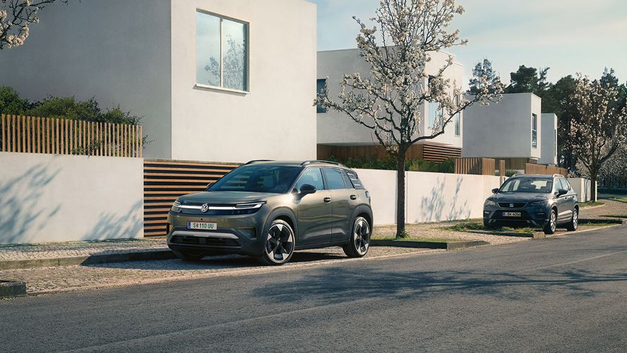 Ein grüner VW ID. Cross parkt in einer Parkbucht eines Wohngebiets mit blühenden Bäumen.