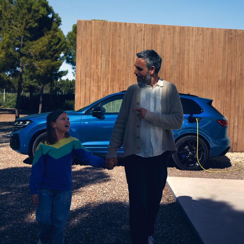 Ein VW Touareg R eHybrid wird geladen, ein Mann und ein Mädchen bewegen sich vom Fahrzeug fort