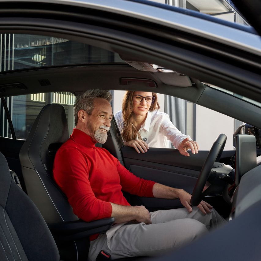 Ein Mann sitzt am Steuer eines Volkswagen und lächelt