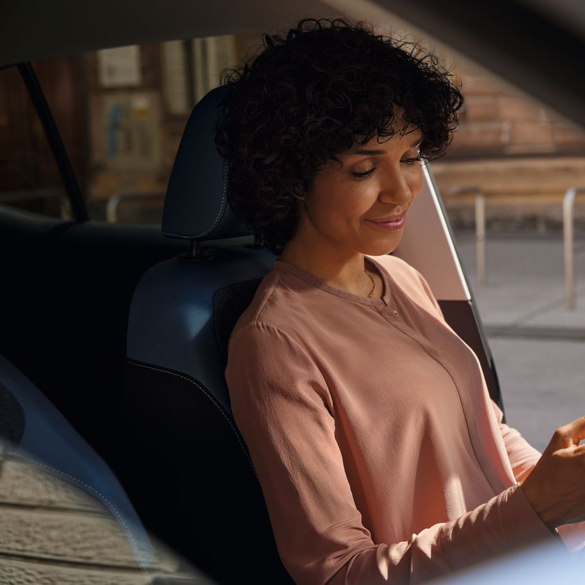 Eine lächelnde Frau schaut auf dem Fahrersitz eines geparkten VW T-Cross aufs Handy.
