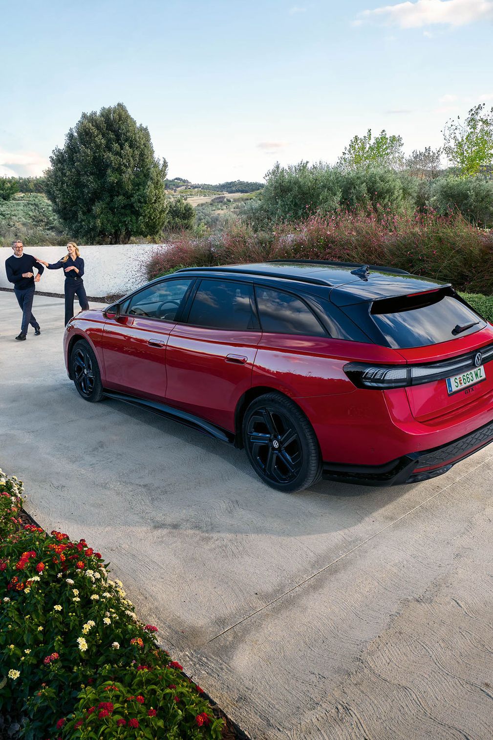 Roter ID.7 Tourer GTX geparkt in einer Einfahrt, ein Pärchen läuft vor dem Auto