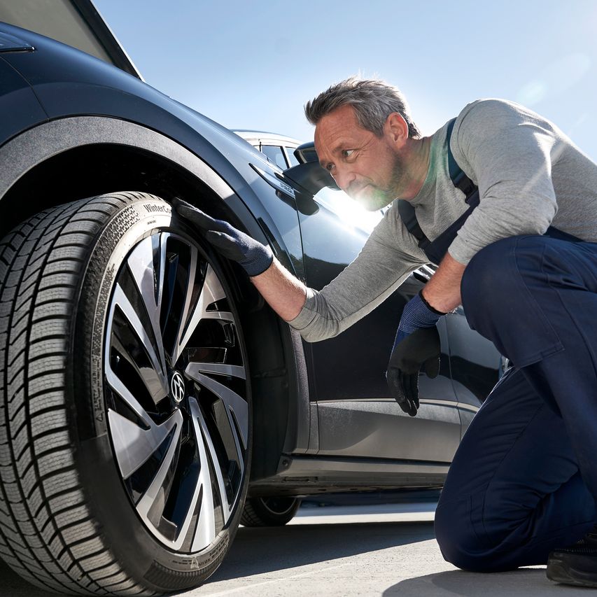 Mechaniker beim Prüfen der Reifen eines VW Fahrzeuges