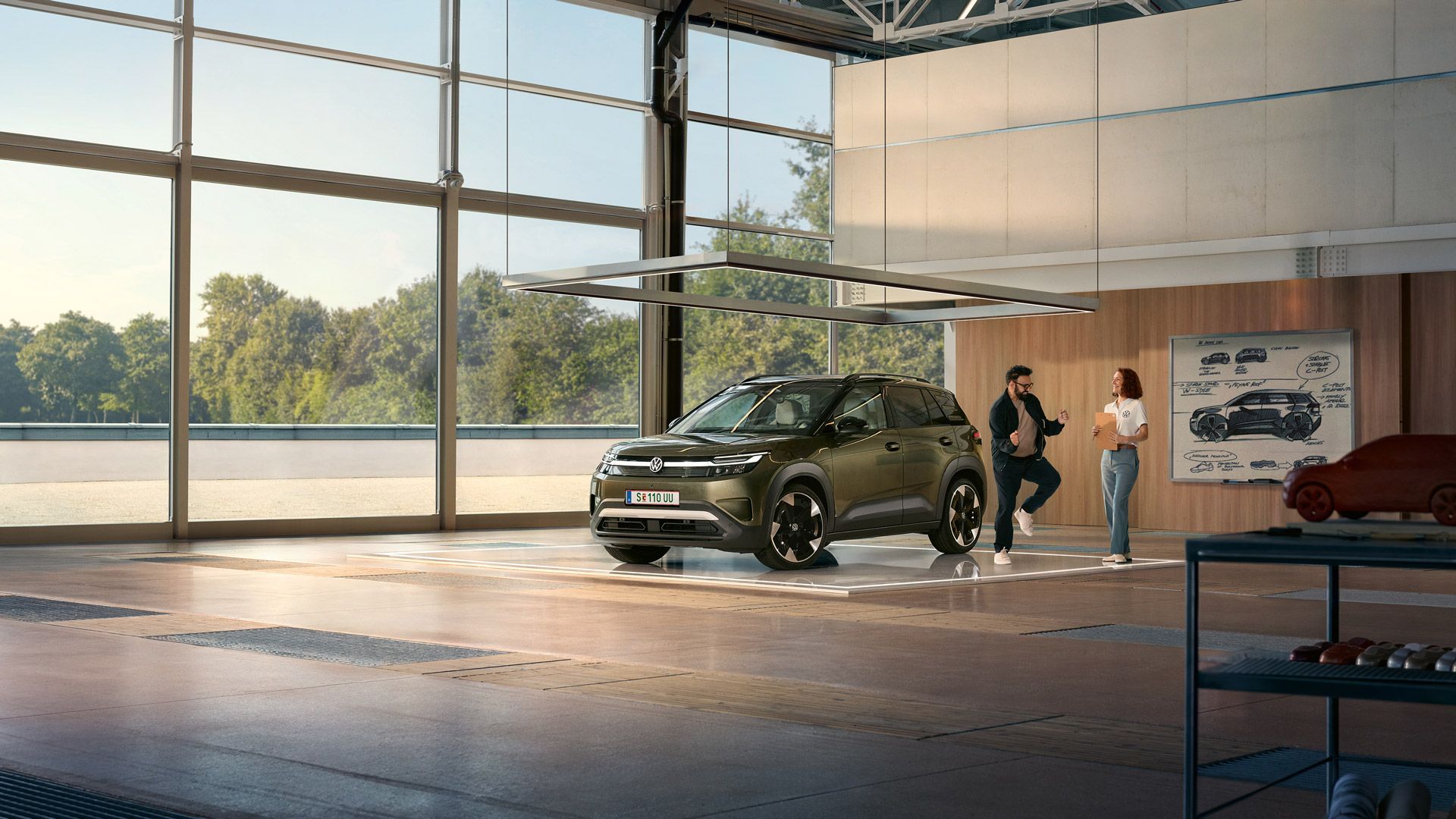 Ein VW ID. Cross steht in einem minimalistisch eingerichteten Designstudio, daneben tänzelt ein aufgeregter Mann und unterhält sich mit einer Ingenieurin.