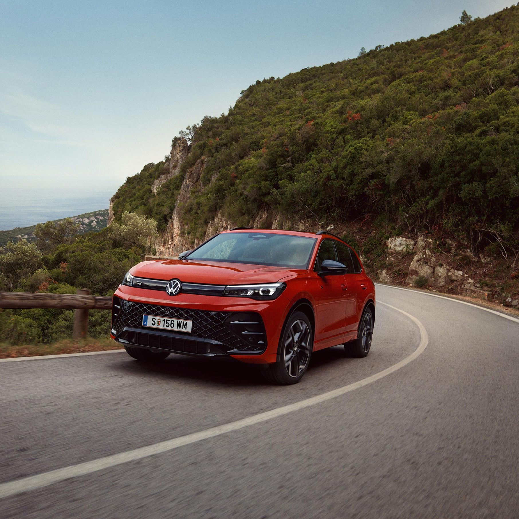 Roter VW Tiguan R-Line fährt eine kurvige Straße entlang.