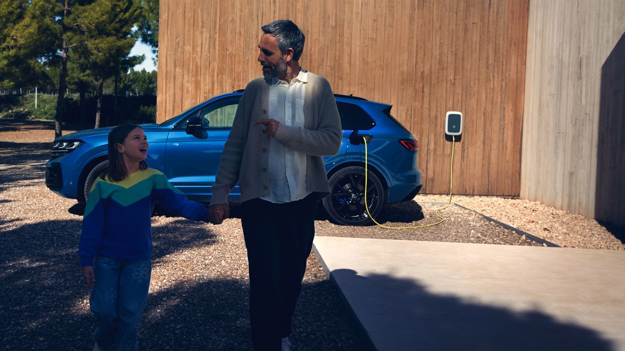 Ein VW Touareg R eHybrid wird geladen, ein Mann und ein Mädchen bewegen sich vom Fahrzeug fort