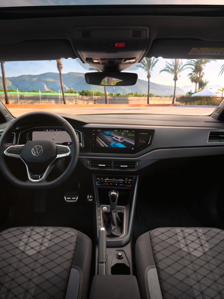 Interieur des VW Taigo mit Digital Cockpit Pro und Infotainmentsystem, Blick durch die Windschutzscheibe auf einen Parkplatz mit Palmen 