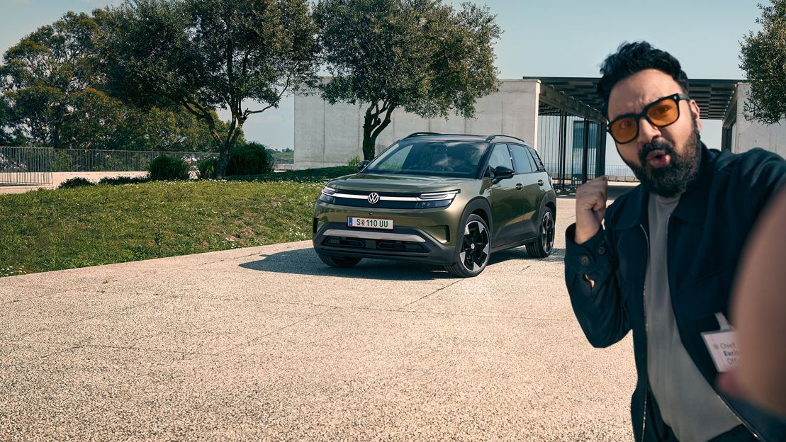 Ein Mann macht ein Selfie mit einem grünen VW ID. Cross, der auf der Auffahrt eines Gebäudes parkt.
