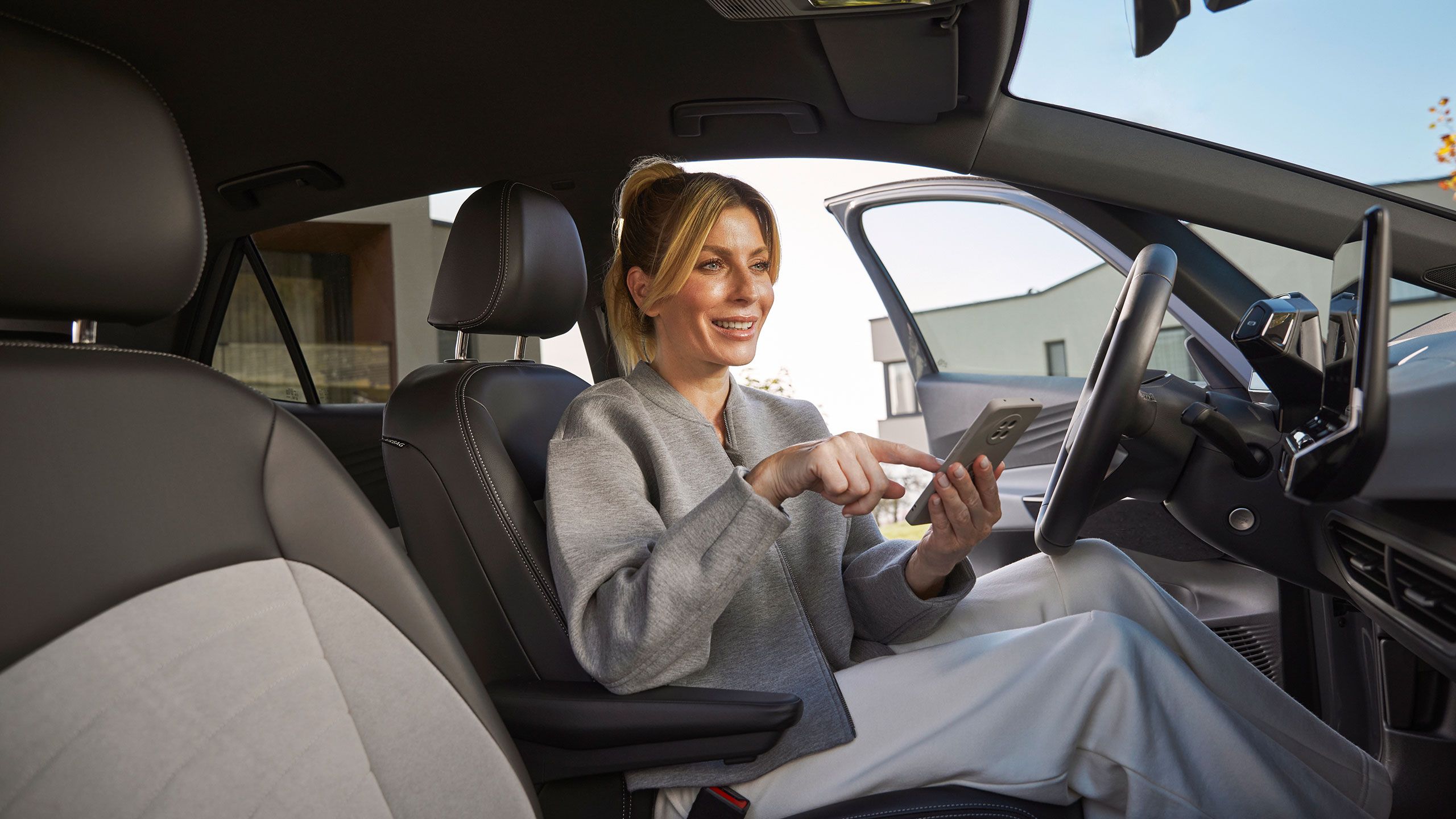 Eine Frau sitzt in einem Volkswagen auf dem Fahrersitz und bedient ein Smartphone. Der Innenraum des Autos wirkt hochwertig. 