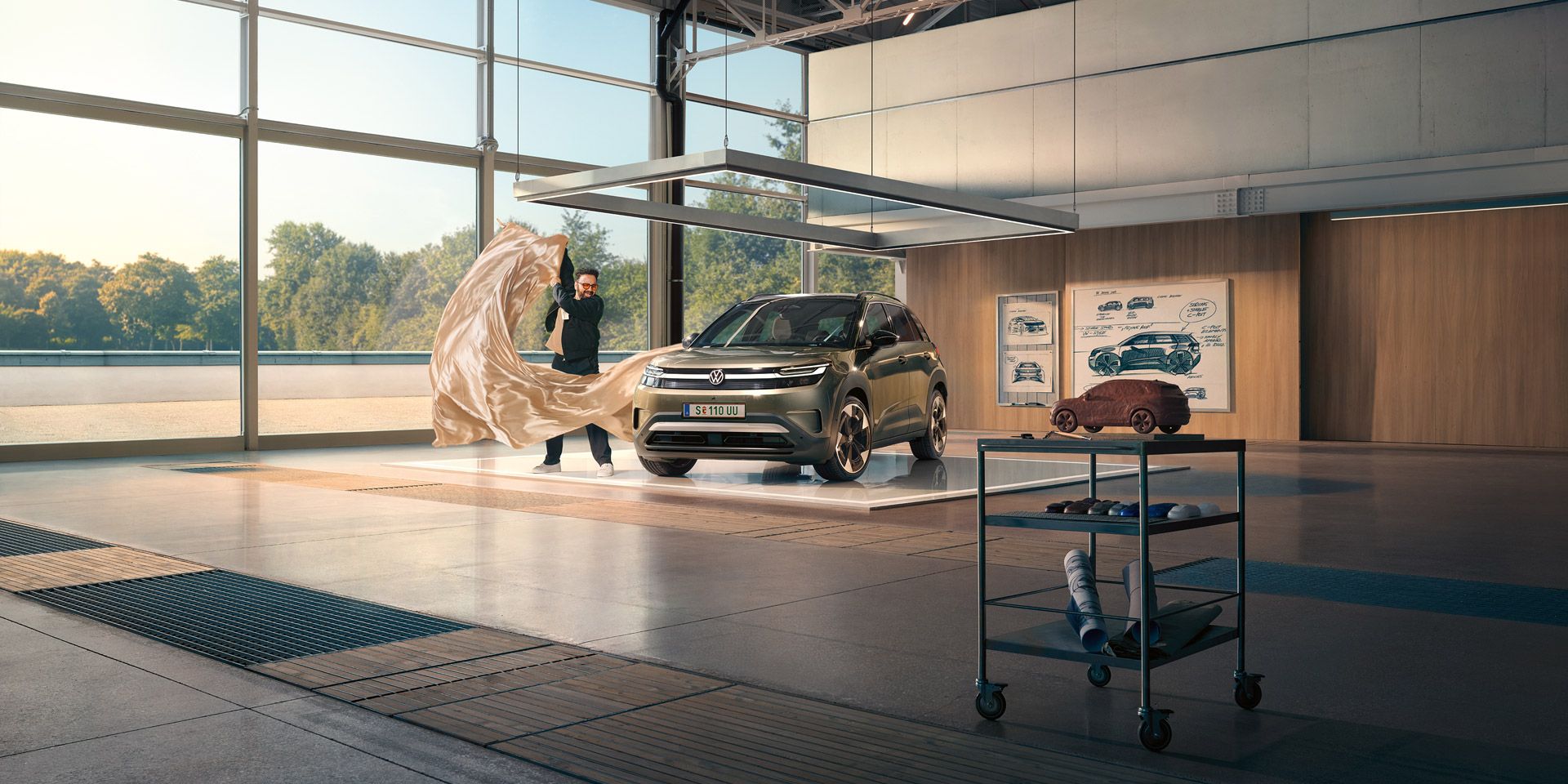 Ein Mann zieht ein großes Tuch von einem grünen VW ID. Cross, der in einem minimalistisch eingerichteten Designstudio steht.