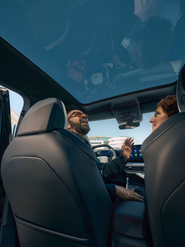 Ein Mann sitzt lachend auf dem Fahrersitz eines VW ID. Cross und schaut durch das geöffnete Panoramadach, eine Frau sitzt auf dem Beifahrersitz.