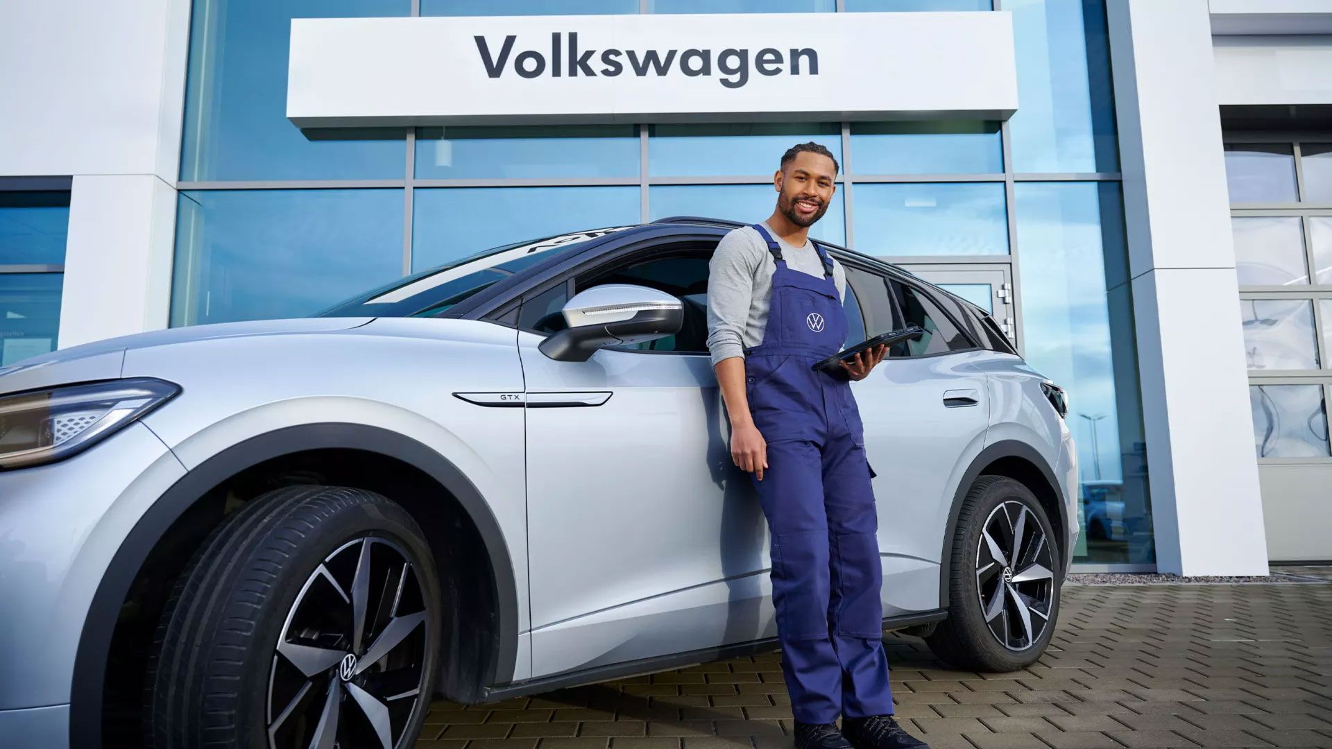 Ein Servicemitarbeiter mit Tablet in der Hand steht vor einem ID. 4 GTX vor einem Autohaus.