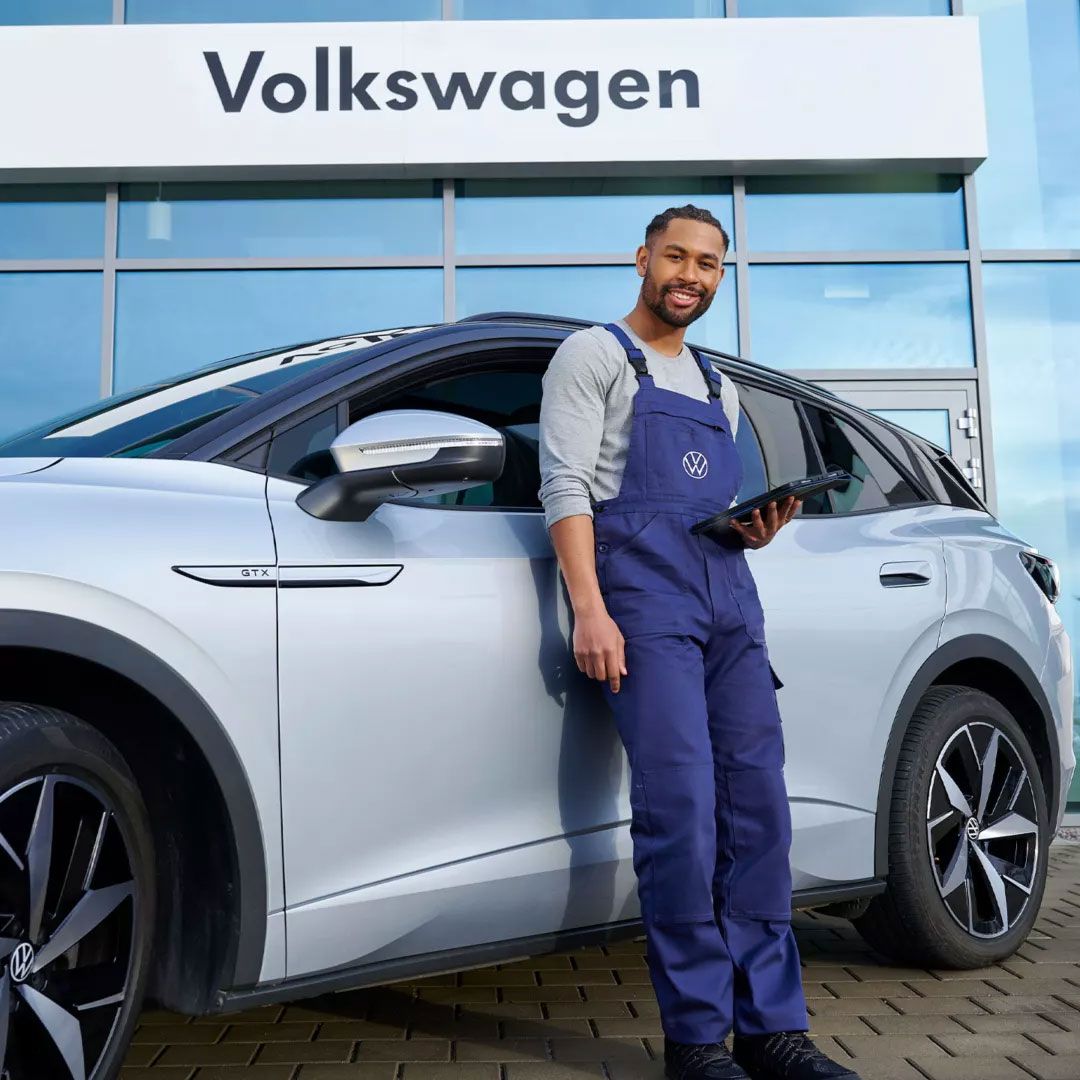 Ein Servicemitarbeiter mit Tablet in der Hand steht vor einem ID. 4 GTX vor einem Autohaus.