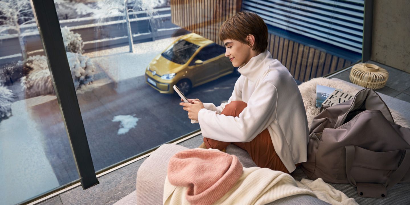 Frau sitzt auf dem Balkon und verbindet sich über das Handy mit ihrem e-up! 