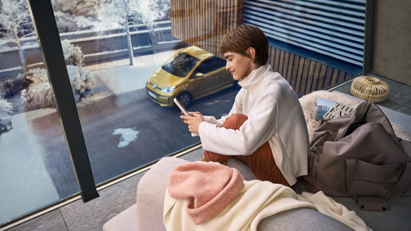 Frau sitzt auf dem Balkon und verbindet sich über das Handy mit ihrem e-up! 