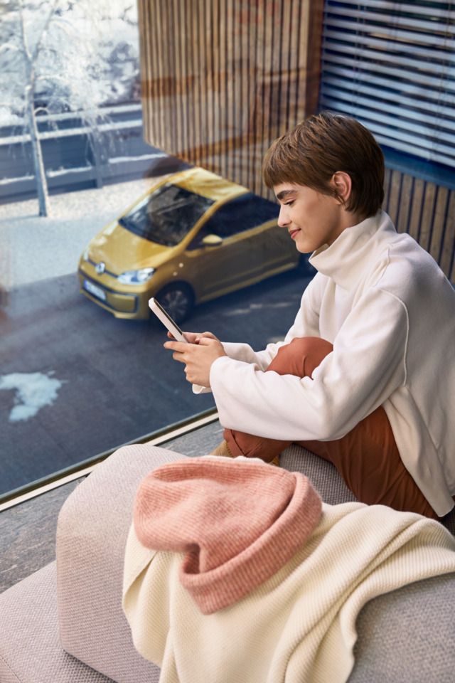 Frau sitzt auf dem Balkon und verbindet sich über das Handy mit ihrem e-up! 
