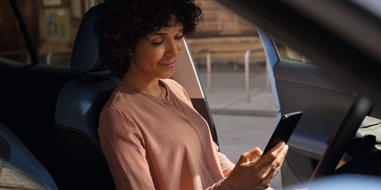 Eine lächelnde Frau schaut auf dem Fahrersitz eines geparkten VW T-Cross aufs Handy.