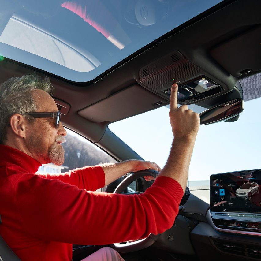 Ein Mann sitzt in einem Volkswagen und bedient das Panoramadach. 