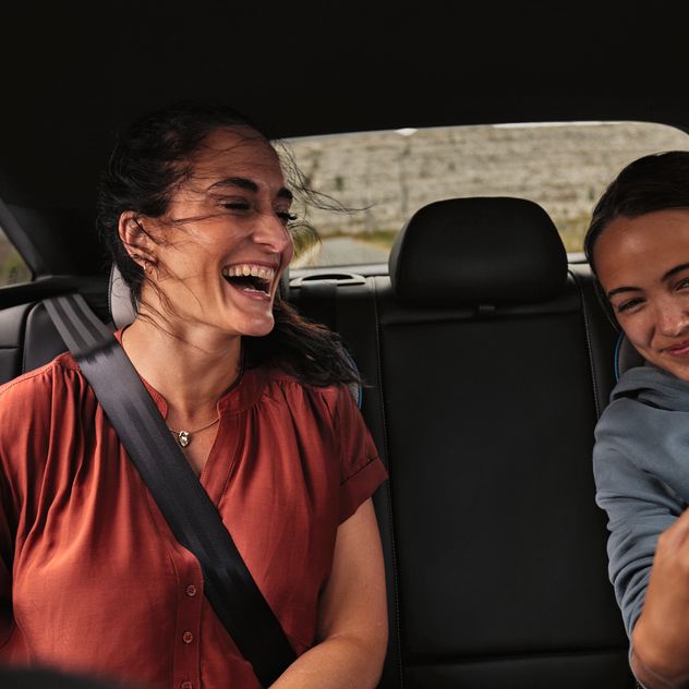 2 Peronen sitzen auf der Rückbank eines Volkswagen und schauen lächelnd auf ein Mobiltelefon