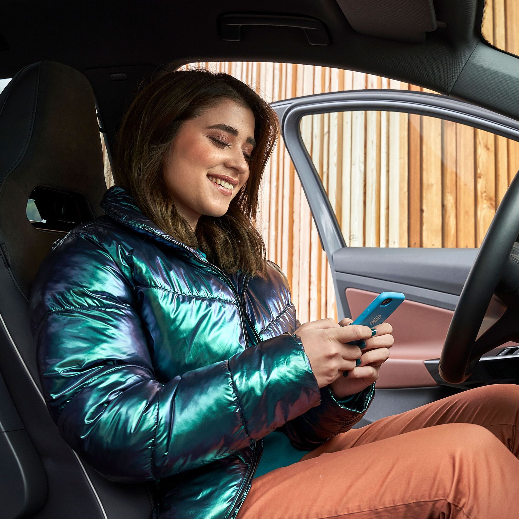 Eine junge Frau sitzt in einem Volkswagen und blickt auf ihr Smartphone