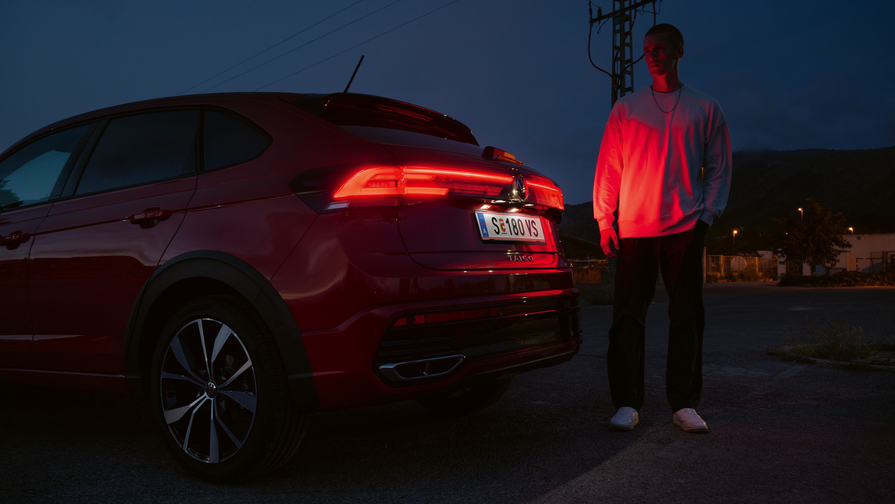 Mann steht hinter VW Taigo, man sieht die durchgehenden IQ.LIGHT LED-Rückleuchten