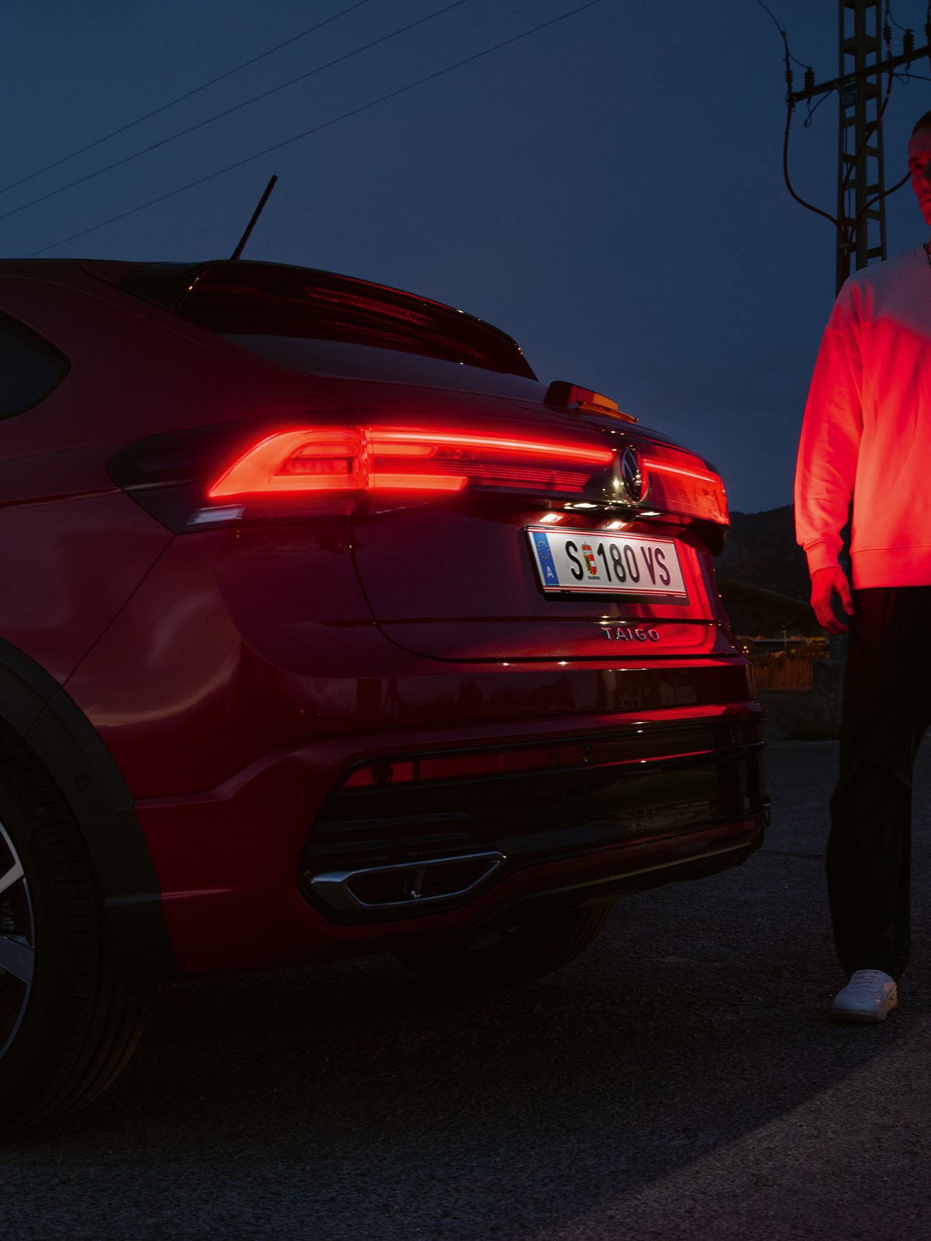 Mann steht hinter VW Taigo, man sieht die durchgehenden IQ.LIGHT LED-Rückleuchten