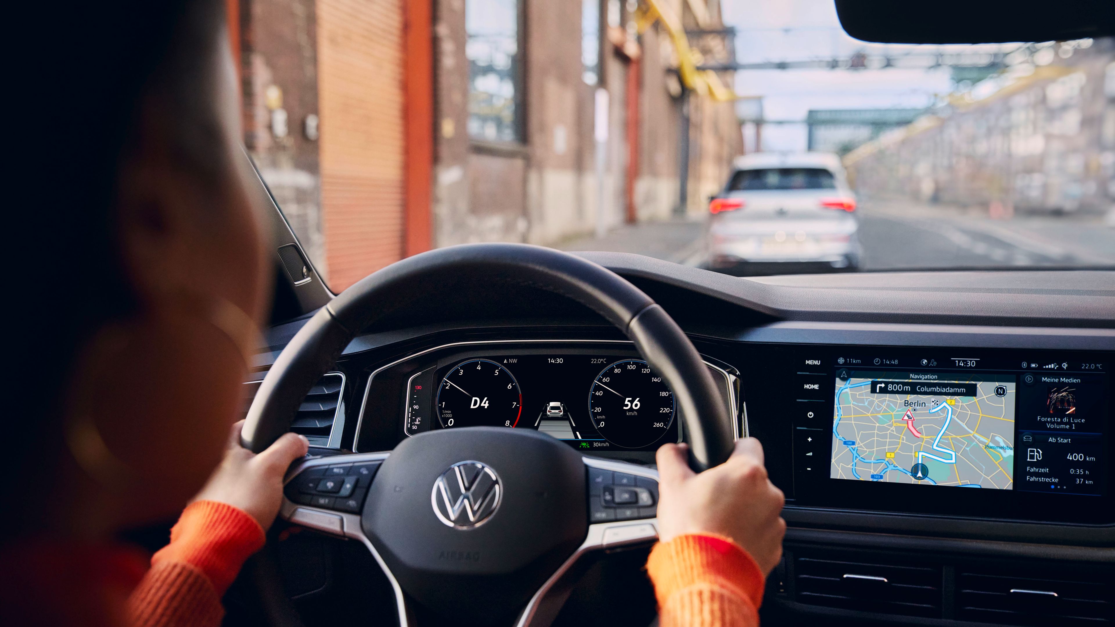 Aktives Navigationssystem auf dem Display eines VW. Frau hat ihre Hände am Lenkrad.