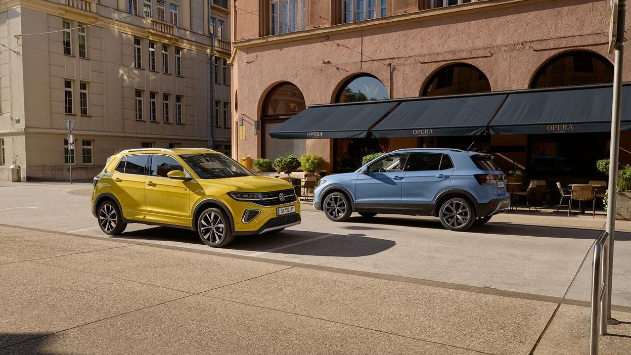 Ein gelber und ein blauer VW T-Cross fahren auf einer Straße aneinander vorbei.
