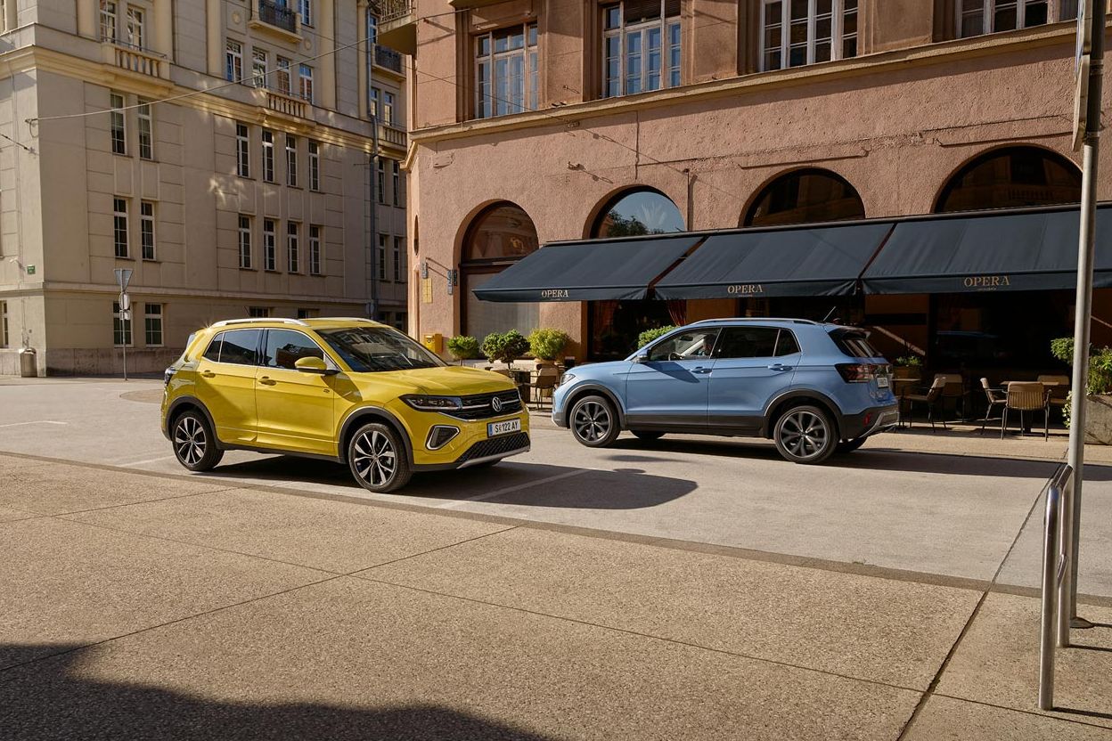 Ein gelber und ein blauer VW T-Cross fahren auf einer Straße aneinander vorbei.