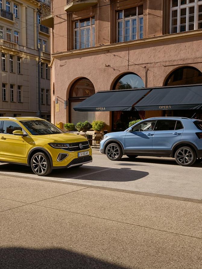 Ein gelber und ein blauer VW T-Cross fahren auf einer Straße aneinander vorbei.