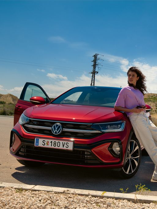 Frau lehnt an einem roten VW Taigo R-Line, dahinter ein Mann auf dem Skateboard