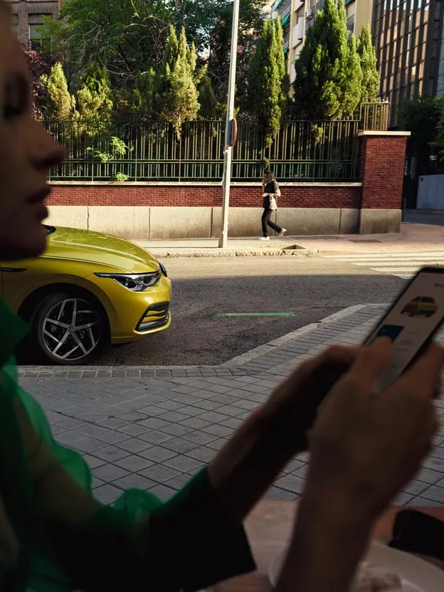 Eine Frau bedient ihr Smartphone, hinter ihr parkt ein VW Golf.