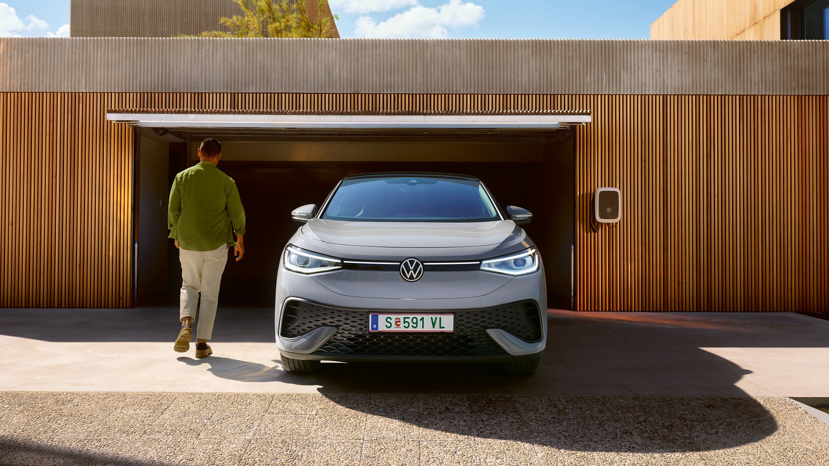 Frontansicht eines grauen VW ID.5 der vor Garage steht, Mann geht an ihm vorbei