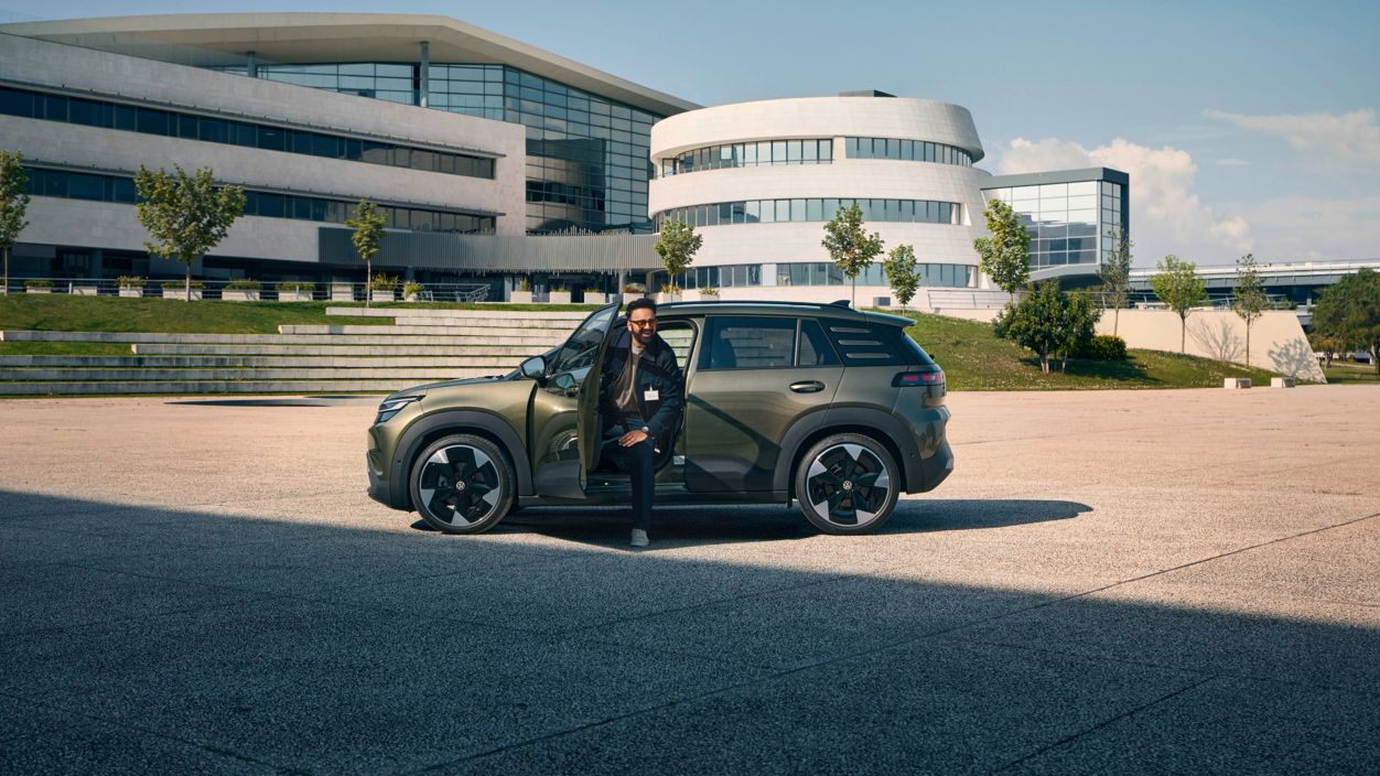 Ein Mann steigt aus der Fahrertür eines VW ID. Cross, der vor einem modernen, mehrstöckigen Firmengebäude steht.