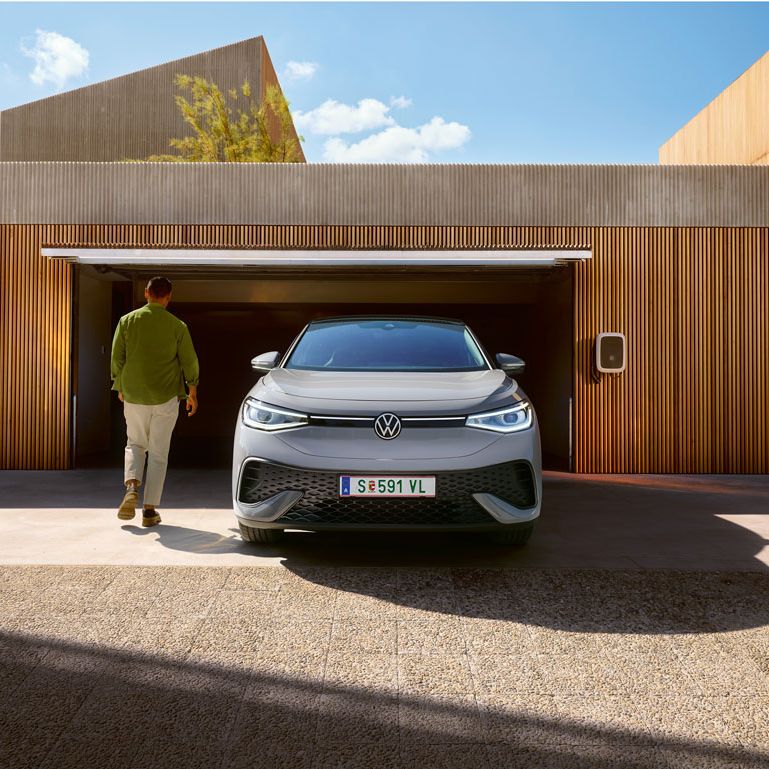 Frontansicht eines grauen VW ID.5 der vor Garage steht, Mann geht an ihm vorbei