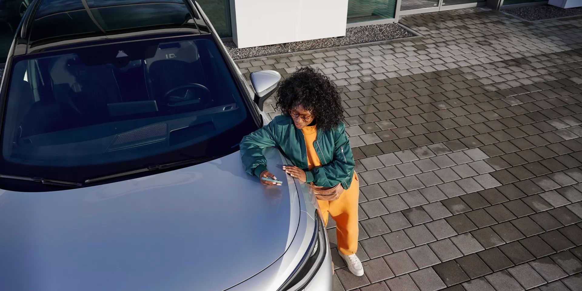 Ein VW ID. mit Blick von oben, eine Frau lehnt an der Kühlerhaube