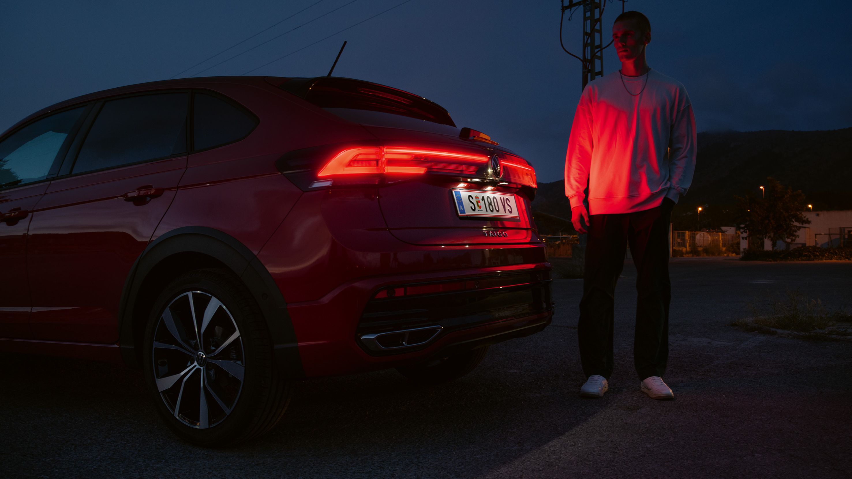 Mann steht hinter VW Taigo, man sieht die durchgehenden IQ.LIGHT LED-Rückleuchten