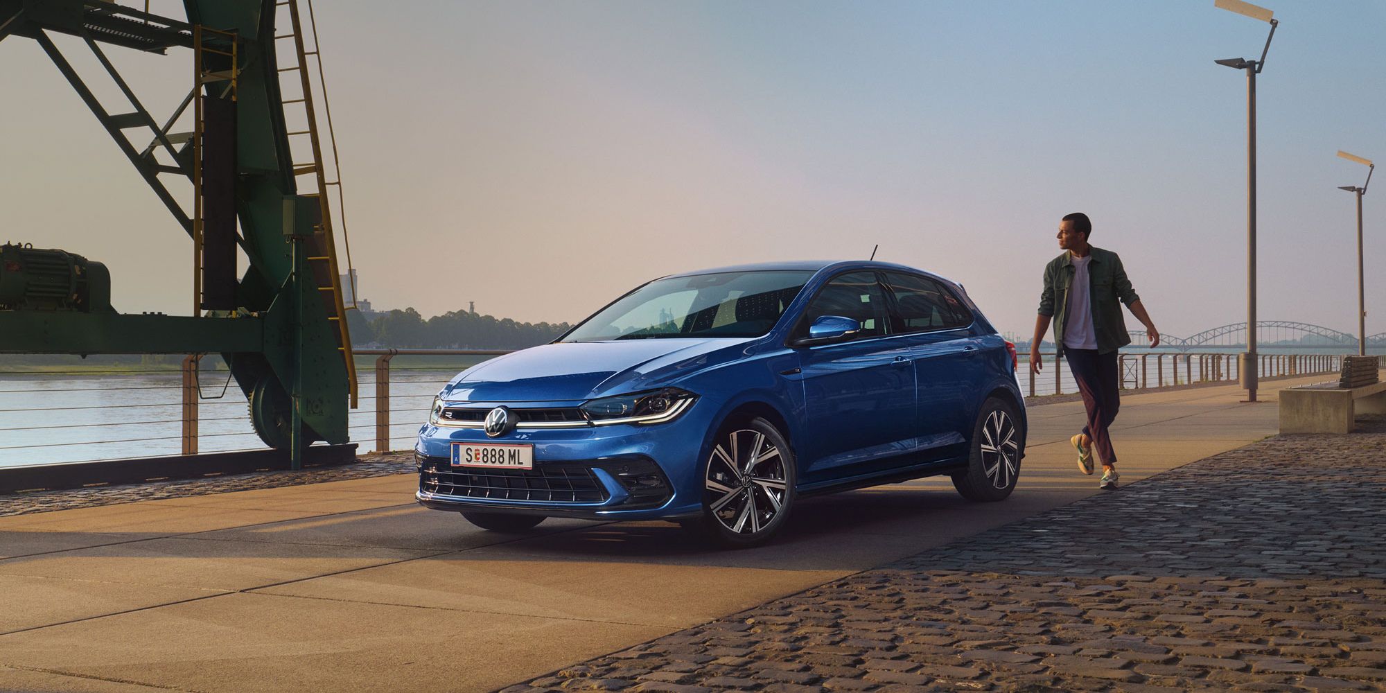 Mann geht an blauen VW Polo R-Line vorbei, der an Promenade geparkt ist