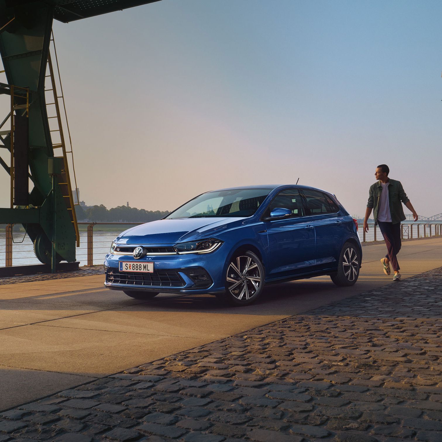 Mann geht an blauen VW Polo R-Line vorbei, der an Promenade geparkt ist