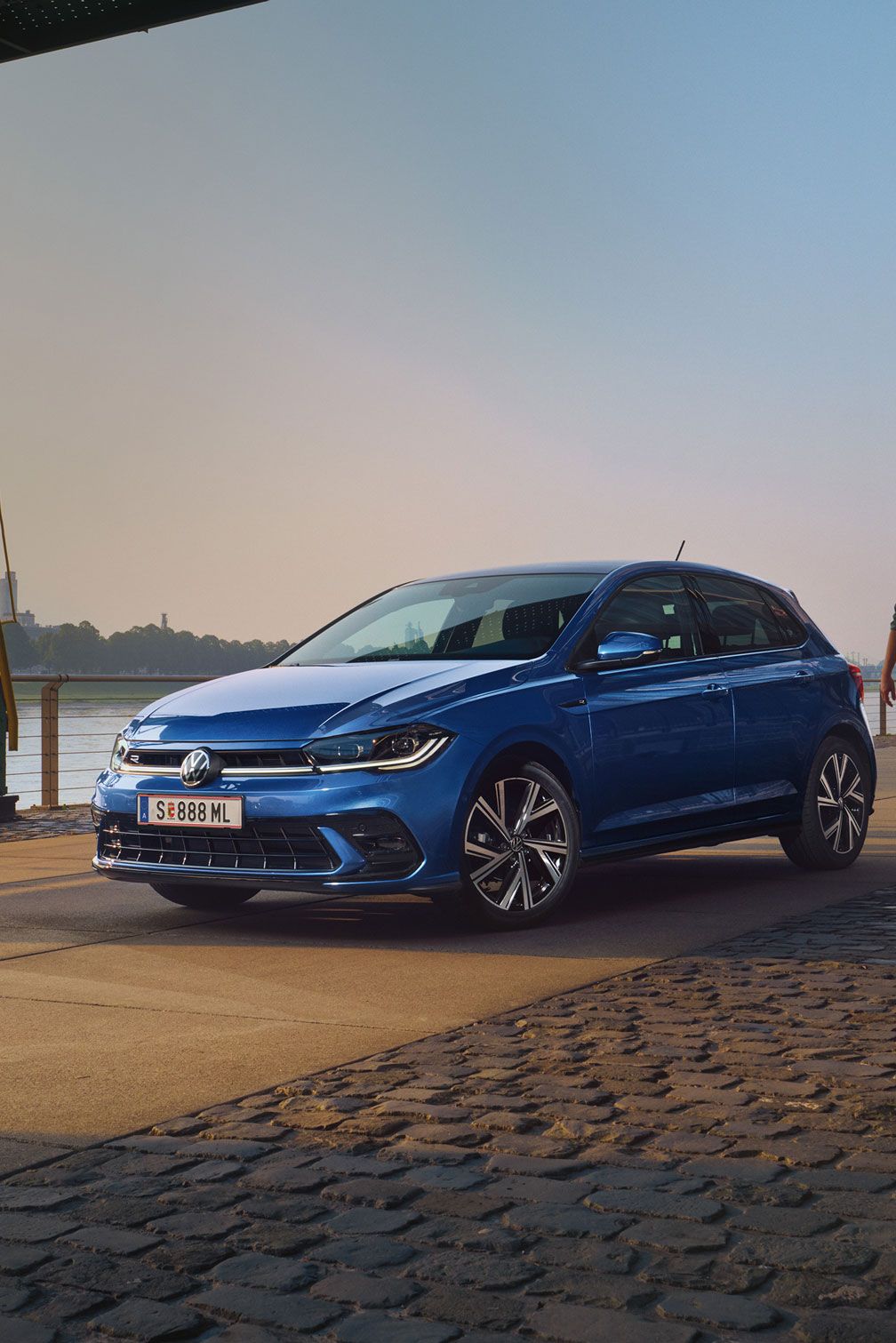 Mann geht an blauen VW Polo R-Line vorbei, der an Promenade geparkt ist